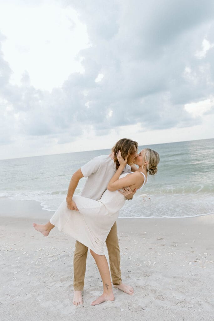 Bride-to-be smiling as her fiancé wraps her in a hug during their Naples engagement photos