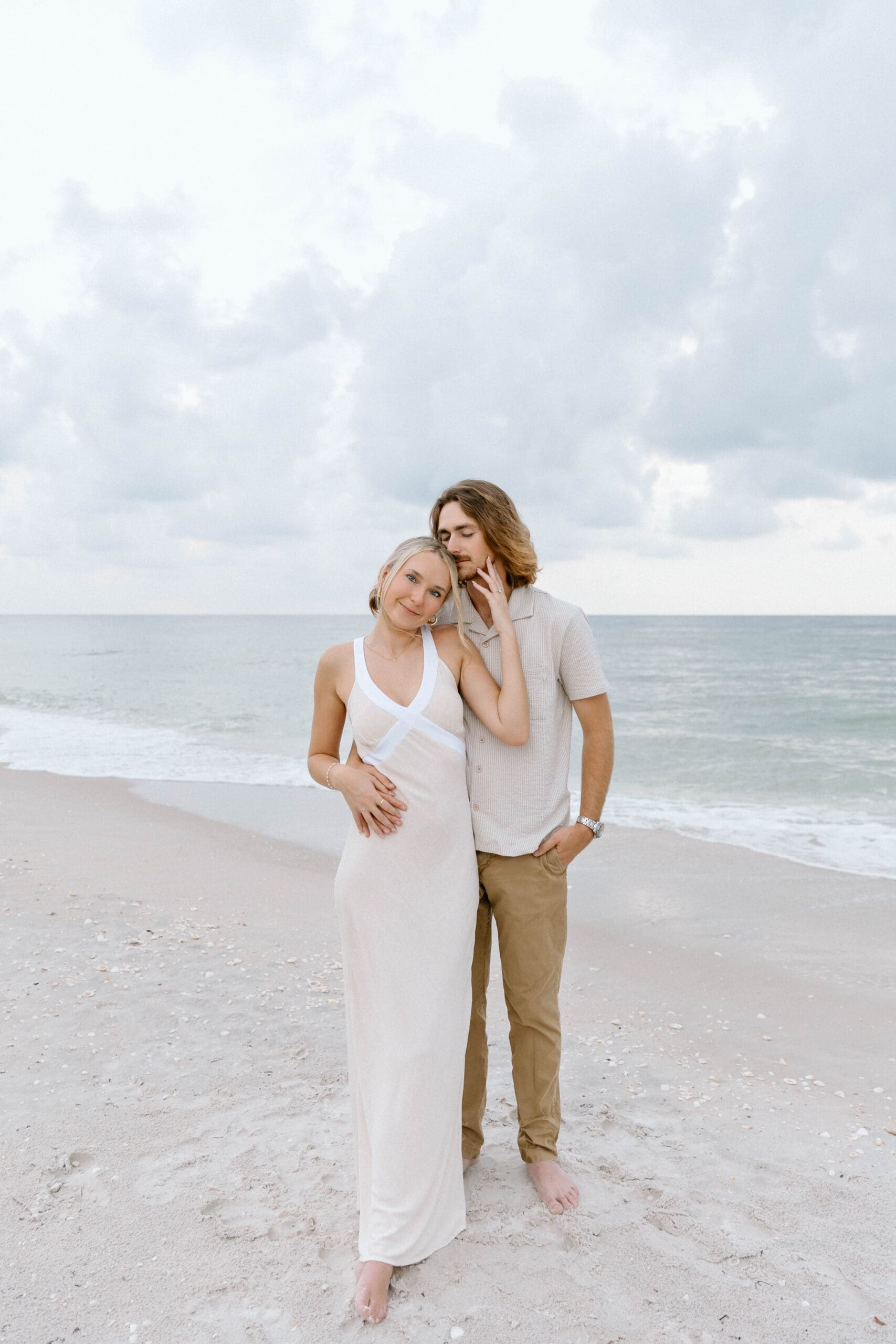 Couple embracing on the beach surrounded by soft gray clouds and coastal tones